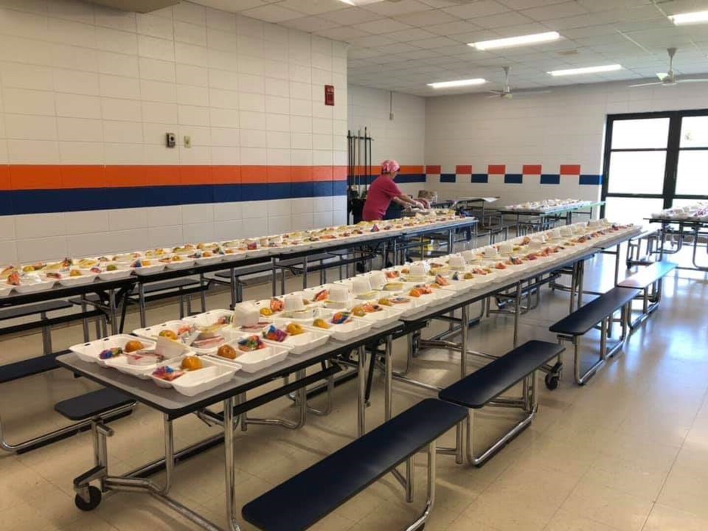 Tables in a school cafeteria are filled with pre-made boxed lunches.