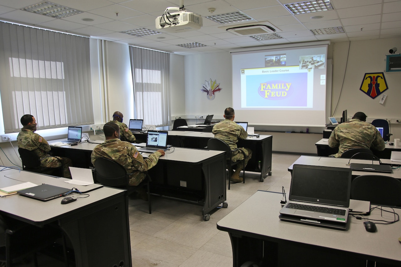 Soldiers sit in a classroom looking at a screen in the front of the room.