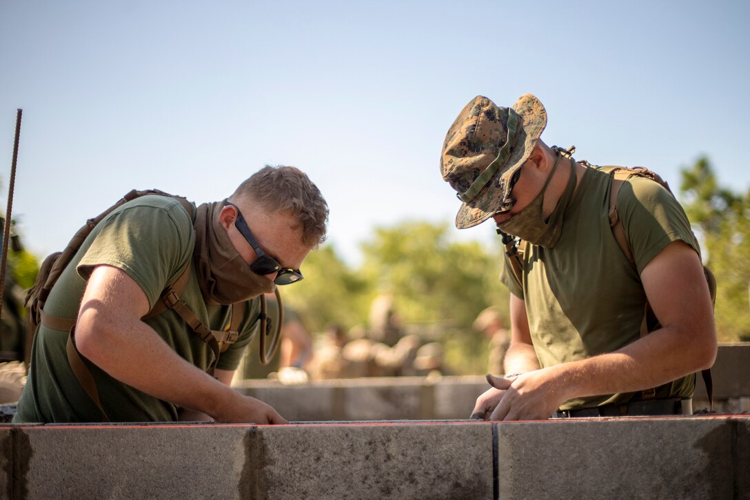 Marines wearing protective gear level a cylinder block wall.