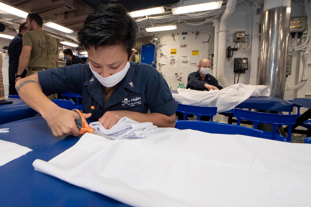 A sailor cuts fabric while making face masks.