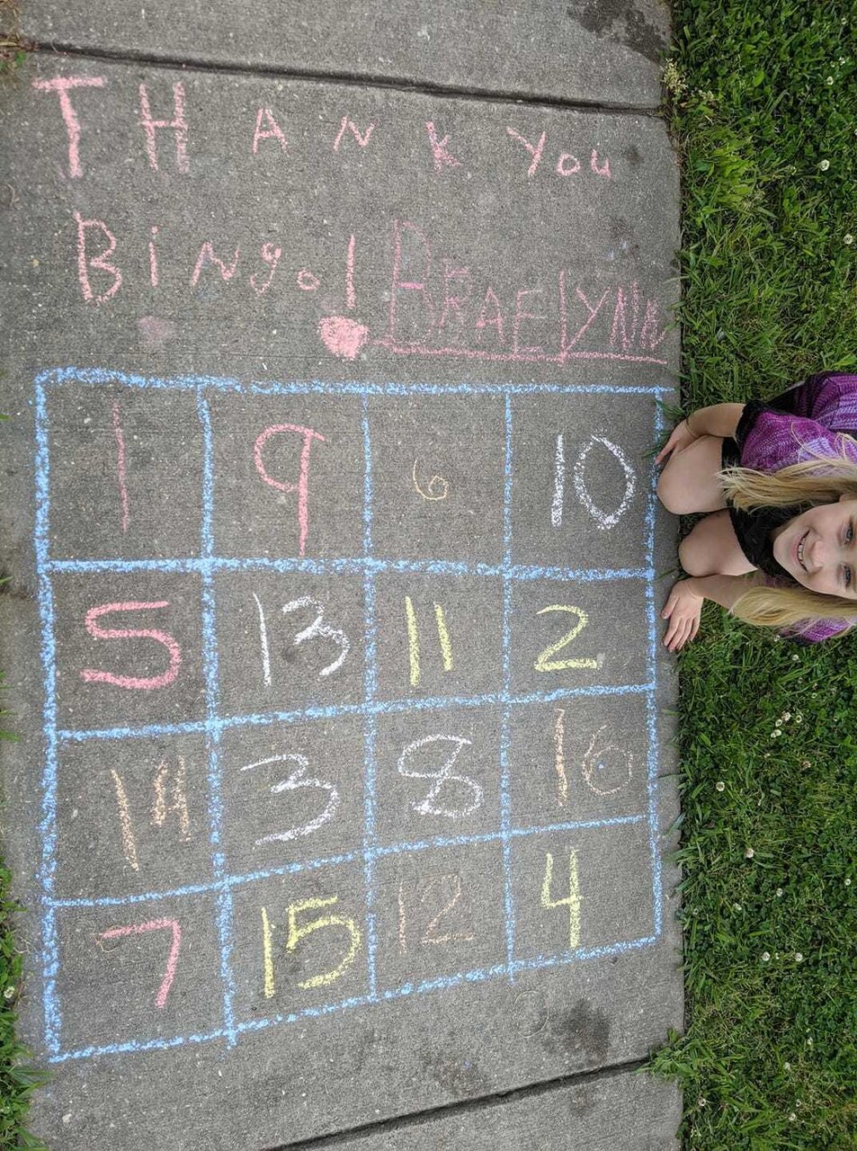 A girl poses with her chalk drawing of a Bingo card with “Thank You Bingo! BraeLynn” inscribed above it.