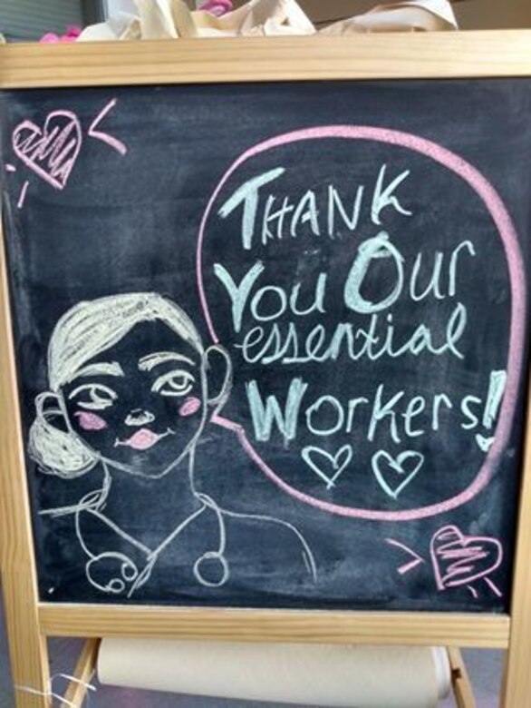 A chalk drawing of a person wearing headphones draped over her shoulders reads, “Thank you our essential workers.”