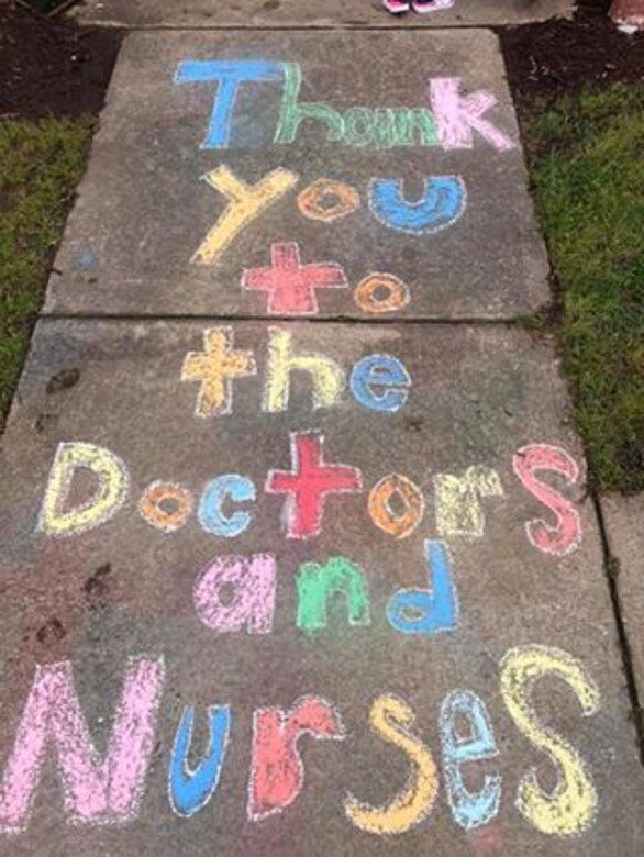 A colorful chalk sign on a sidewalk reads, “Thank you to the Doctors and Nurses.”