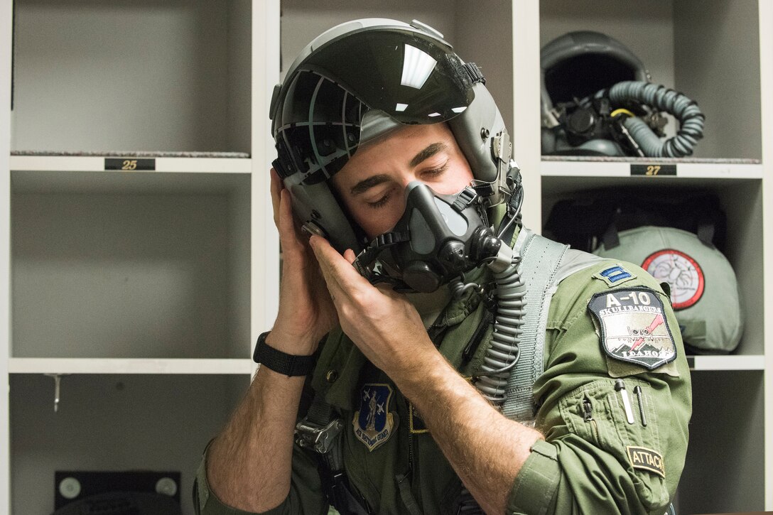 A pilot in a flight suit latches his flight helmet to his head.