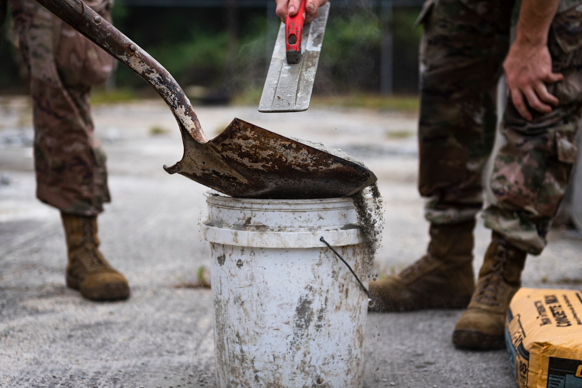 A photo of an Airman adding concrete mix to a bucket.