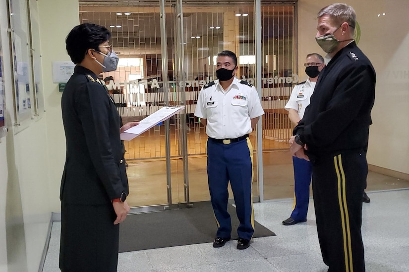 A female officer and a male officer face each other to talk as two other service members look on. All are wearing face masks.