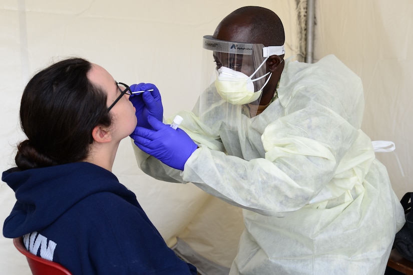 A man wearing personal protective equipment swabs the nose of a young woman.