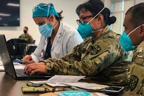 Two soldiers and a hospital personnel, all wearing face masks, work together to assign service members to teams and shifts.