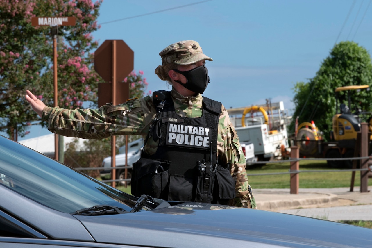 A soldier wearing a face mask and a military police vest directs traffic.