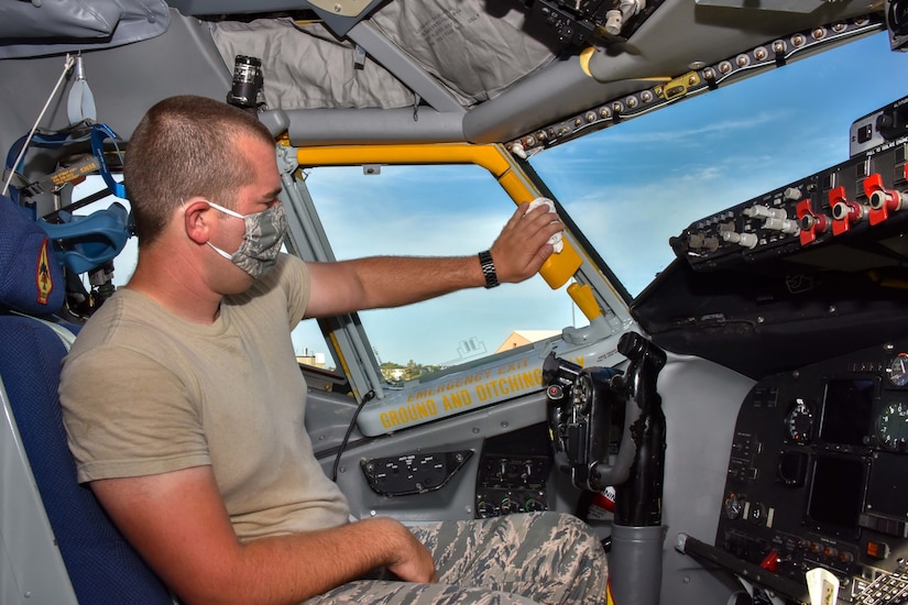 An airman wearing a face mask wipes down the cockpit of a tanker aircraft.