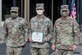 Three soldiers stand side by side while the soldier in the middle shows a certificate.