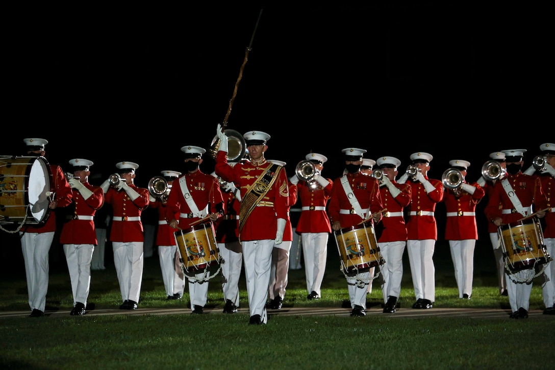 Marines in red uniforms march across a field holding instruments.