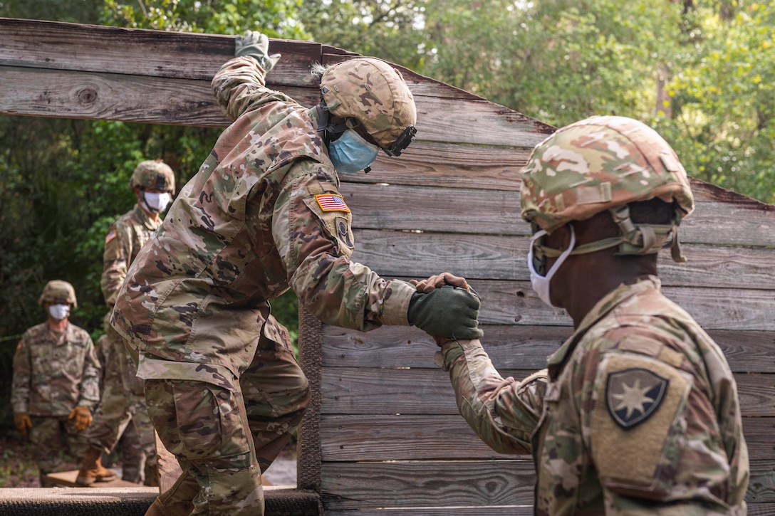 A soldier lends a hand to help another climb down an obstacle course.