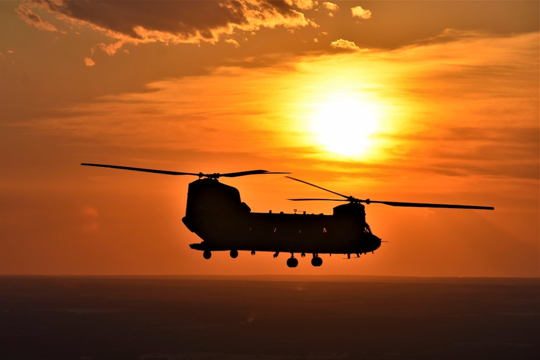 A helicopter flies in the sky as the sun sets behind.