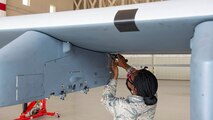 Female mechanic removes bolt from MQ-9 Reaper pylon.