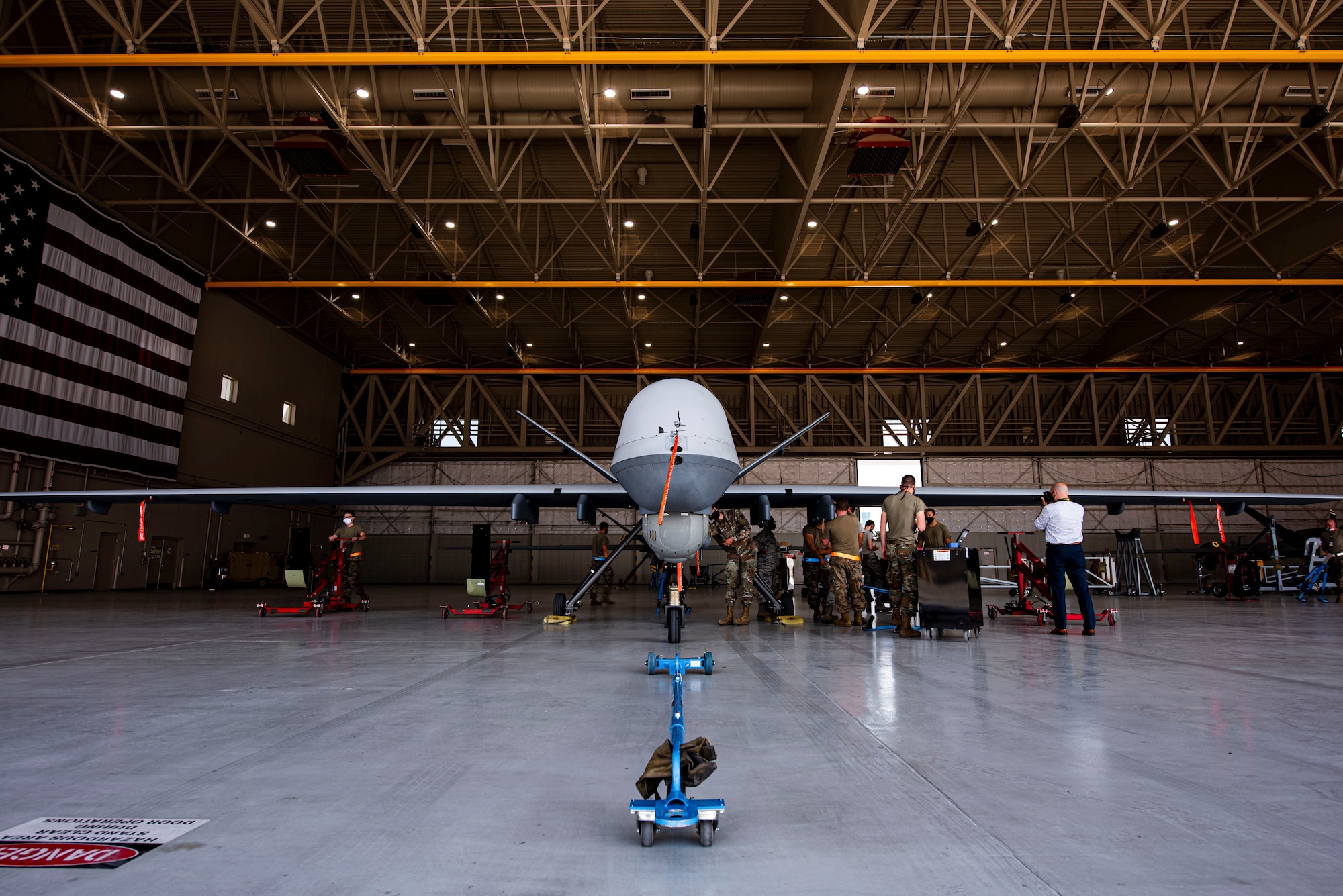 MQ-9 Reaper sits in a hangar with 8 members preparing for routine maintenance.