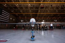 MQ-9 Reaper sits in a hangar with 8 members preparing for routine maintenance.