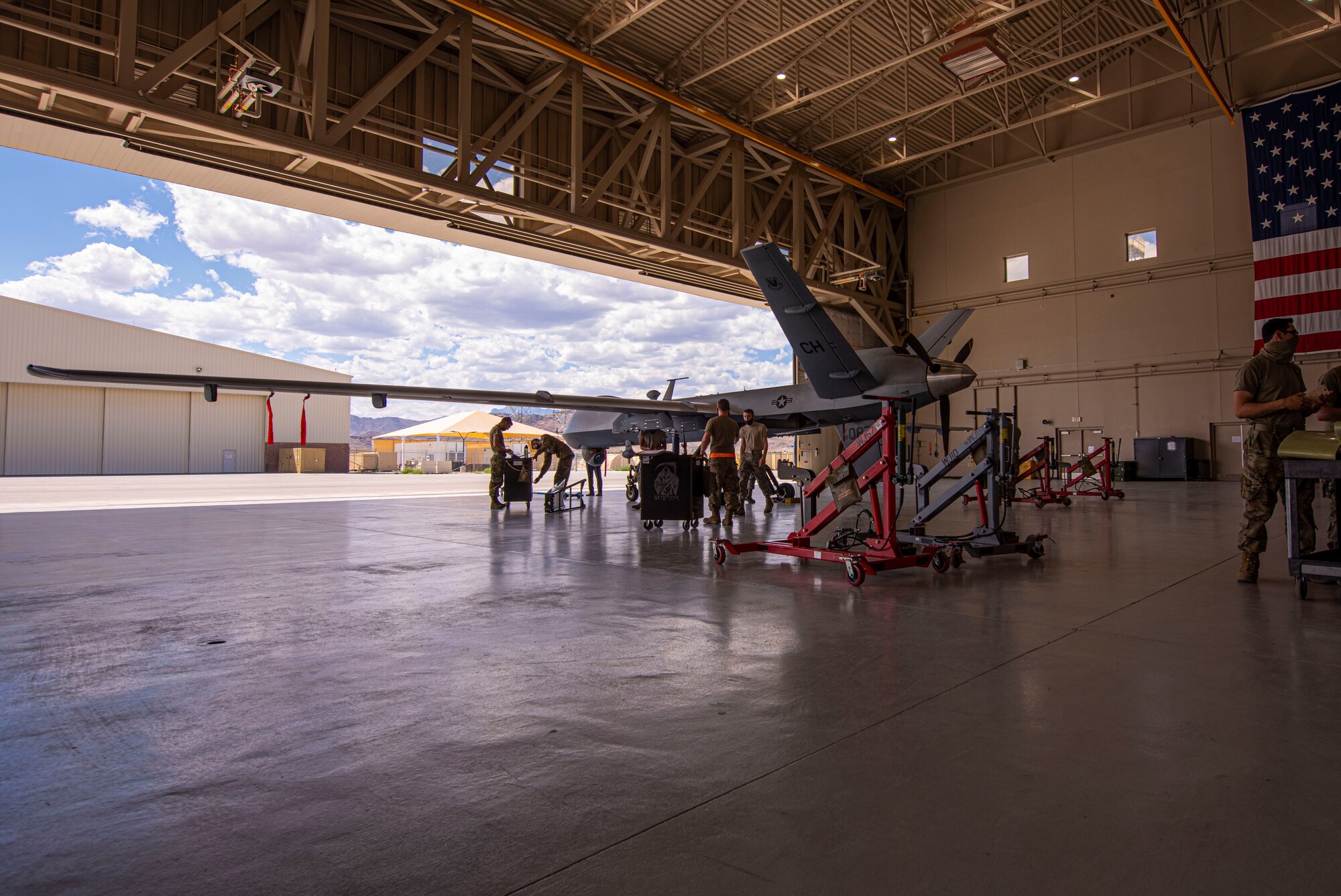 An MQ-9 Reaper sits in a hangar with a crew of 5 members as they prepare for routine maintenance.