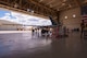 An MQ-9 Reaper sits in a hangar with a crew of 5 members as they prepare for routine maintenance.