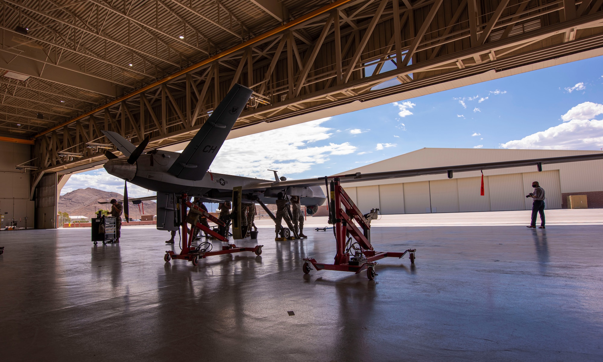 An MQ-9 Reaper sits in a hangar with 5 members preparing to conduct routine maintenance.