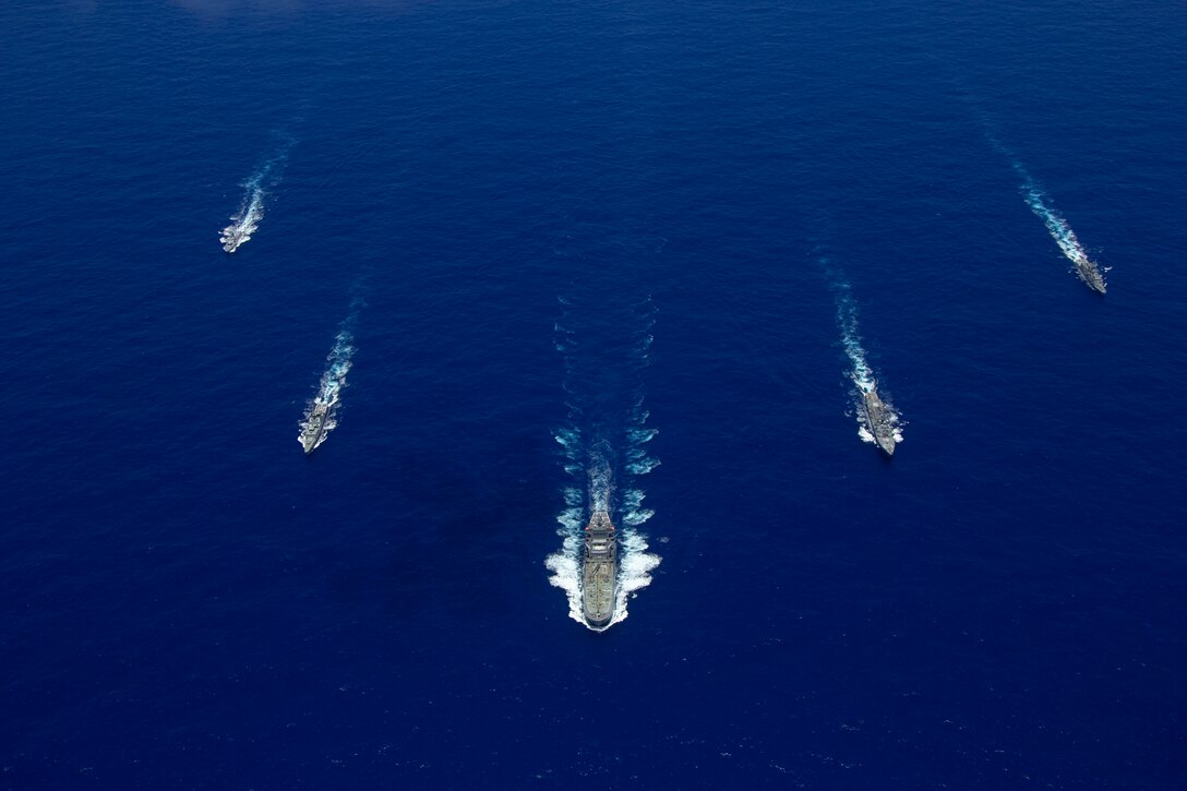 Five ships sail in formation on the ocean.