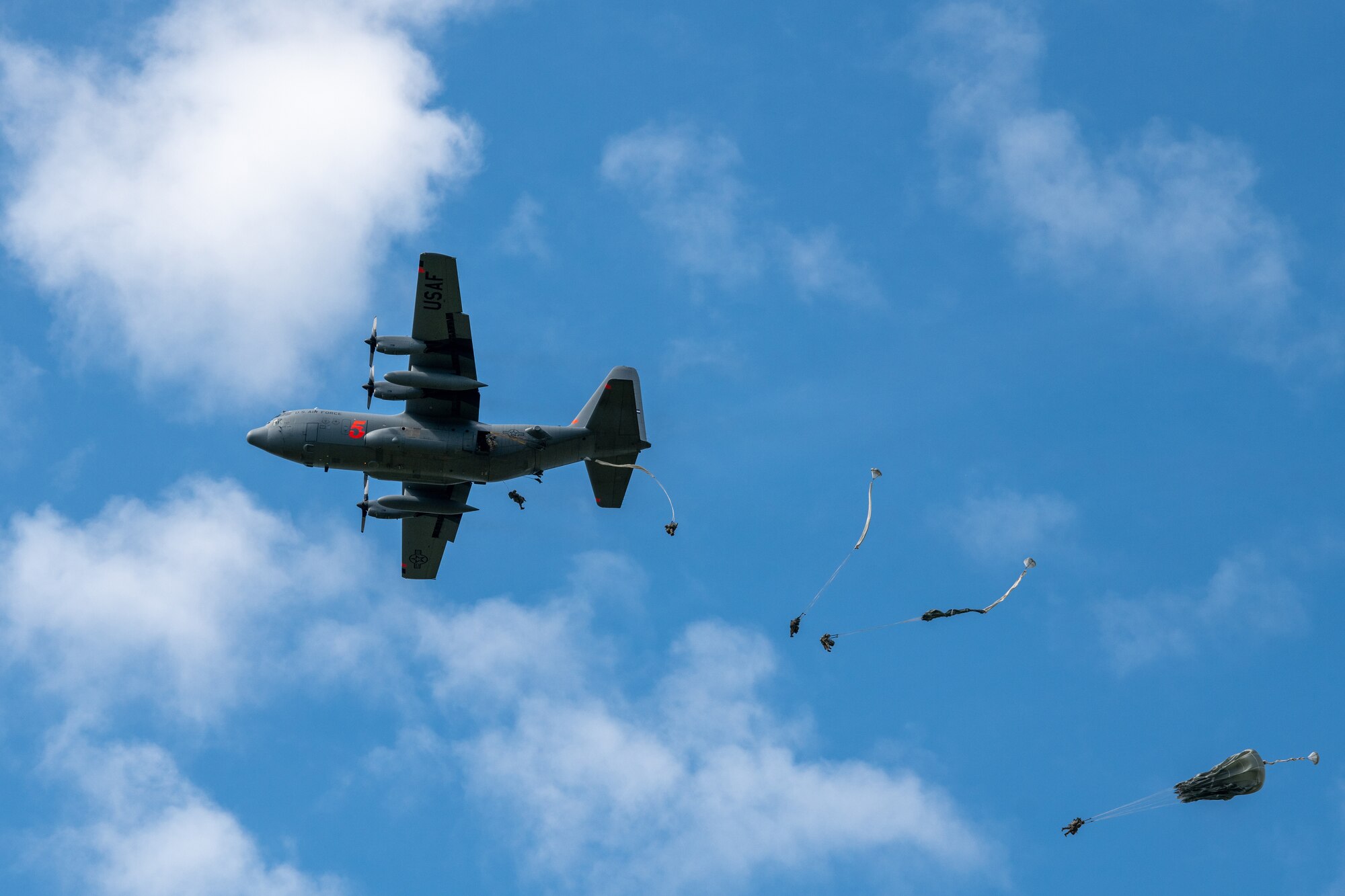 Plane flies through sky, Army soldiers deploy out using parachutes.