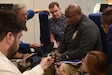 Man sits among five reporters with microphones and notepads.