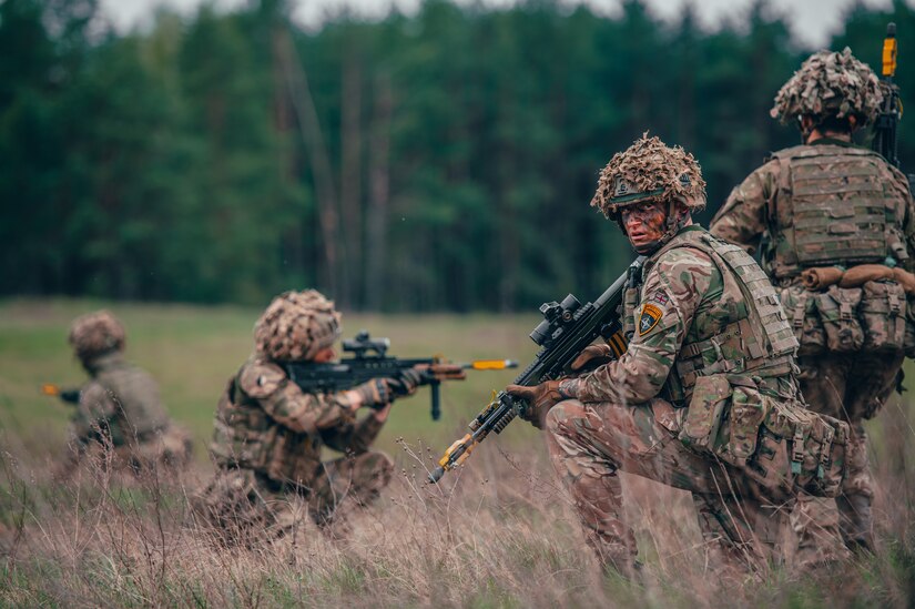 Service members with rifles operate in a field.