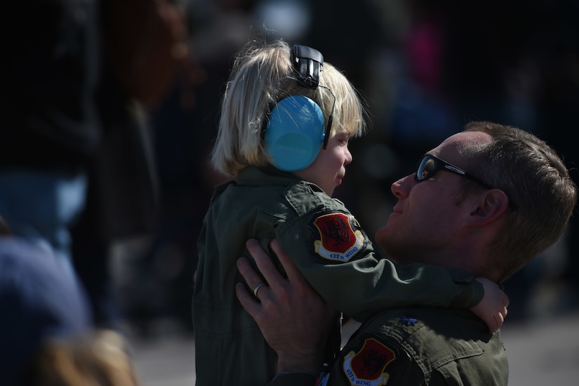 A man wearing a military uniform holds a small boy in the air. The boy is wearing a military uniform similar to that of the man.