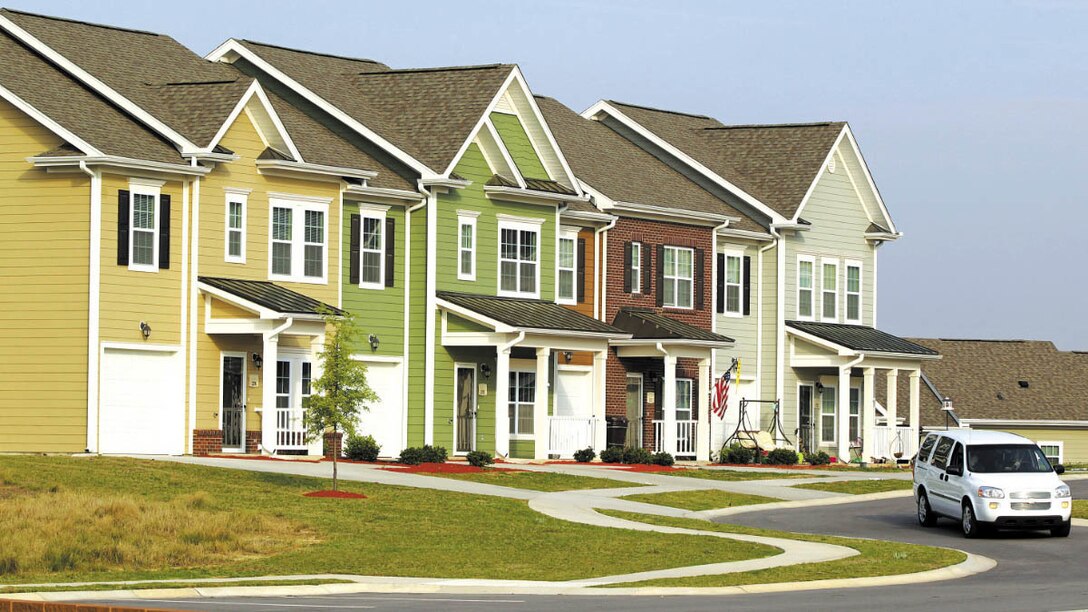 A white van drives in front of a row of homes.