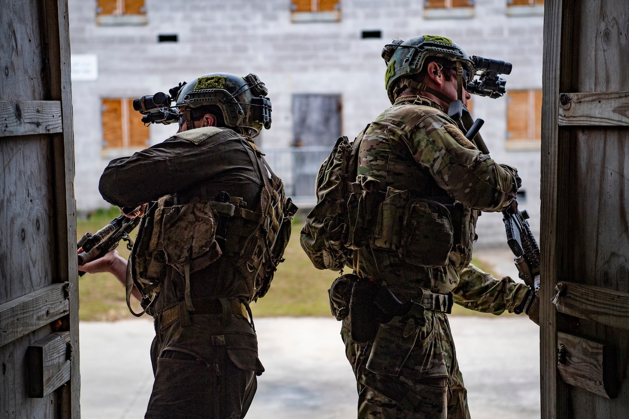 Two service members stand in a doorway and peer out.