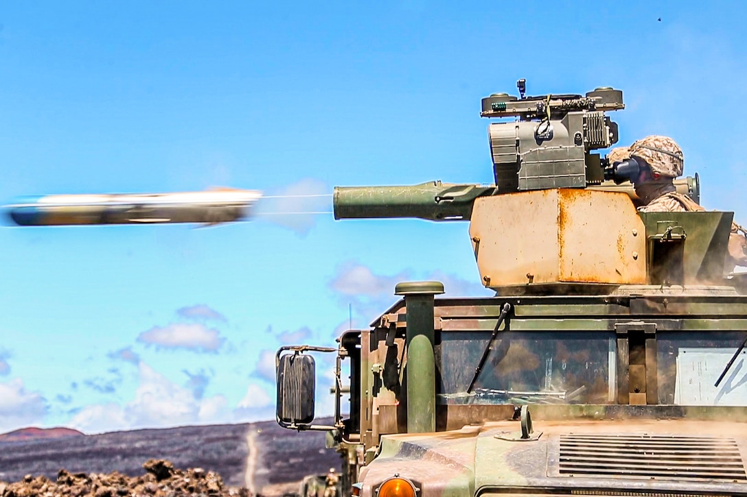 A missile shoots out from the turret of a military vehicle manned by a Marine.