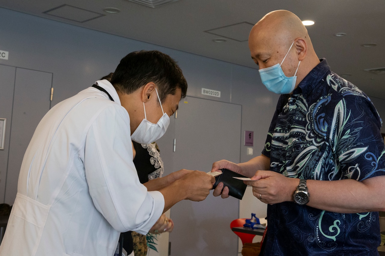 Two men wearing face masks exchange business cards.