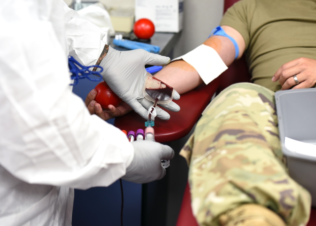 Gloved hands of a technician fill vials with blood from a donor’s arm.