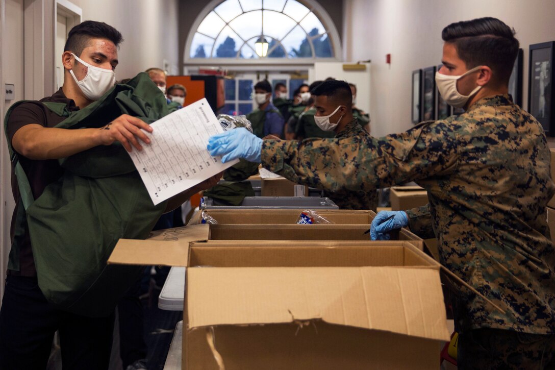 A Marine wearing a face mask and gloves gives a new recruit printed instructions prior to recruit training.