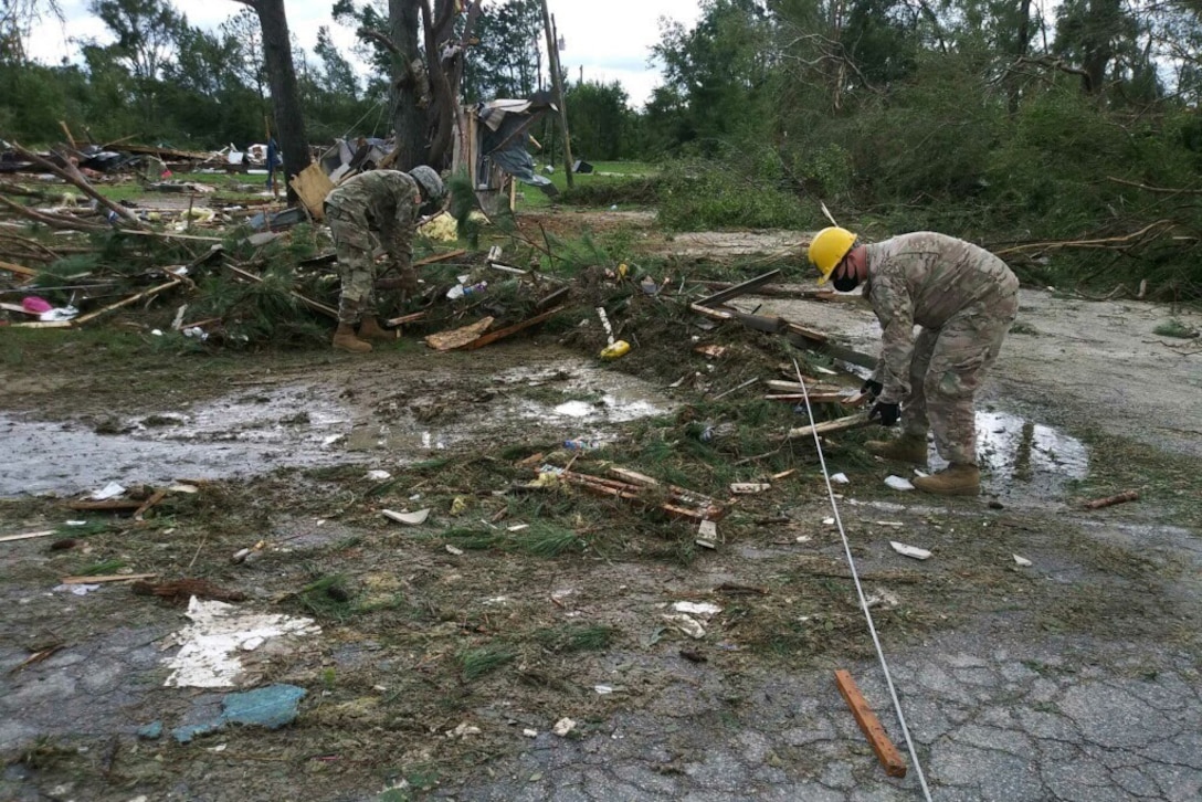 Two soldiers clean up debris scattered across the ground.