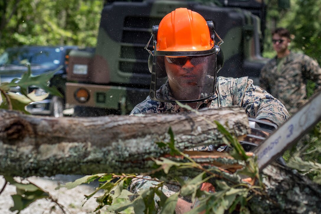A Marine uses a chainsaw to cut tree branches.