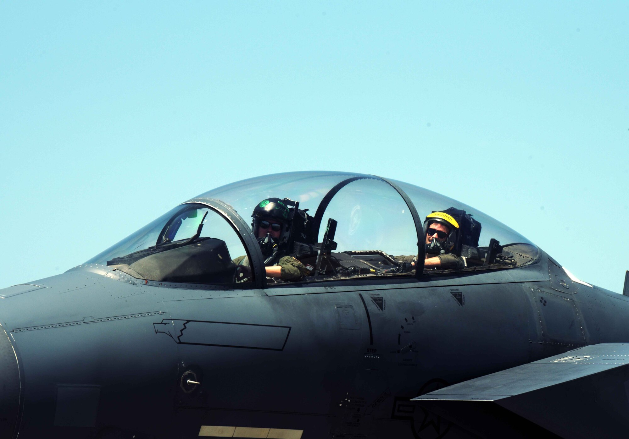 Pilots look out of an F-15E as they taxi on the runway after landing.