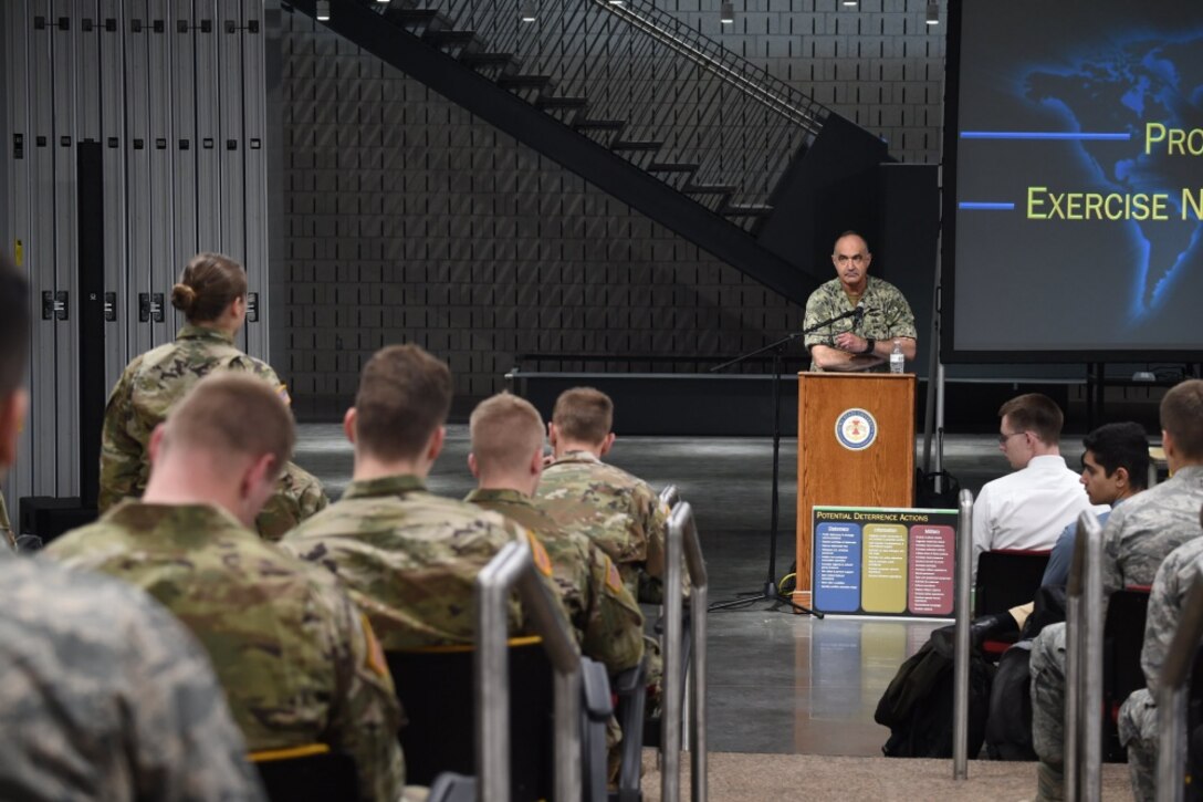 A cadet stands to address an admiral who is standing at a lectern.