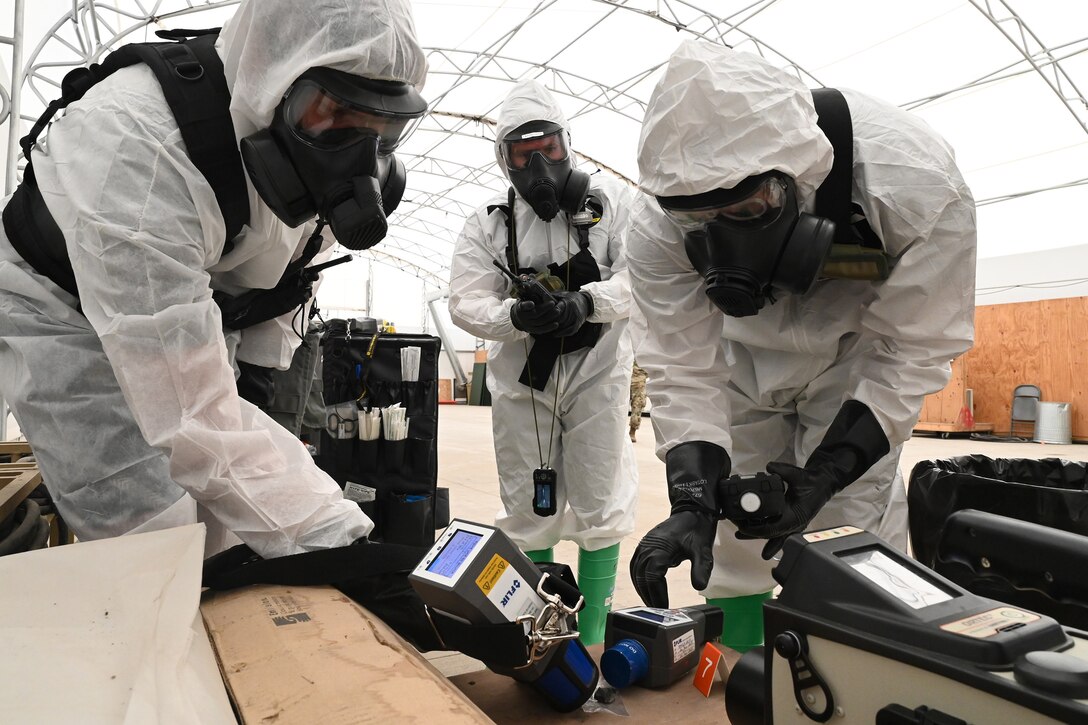 Three N.D. National Guard members wear white protective suits, gas masks, gloves and boots as they look for simulated radioactive material for training during an exercise at the North Dakota Air National Guard Base, Fargo, N.D., Aug 4, 2020.