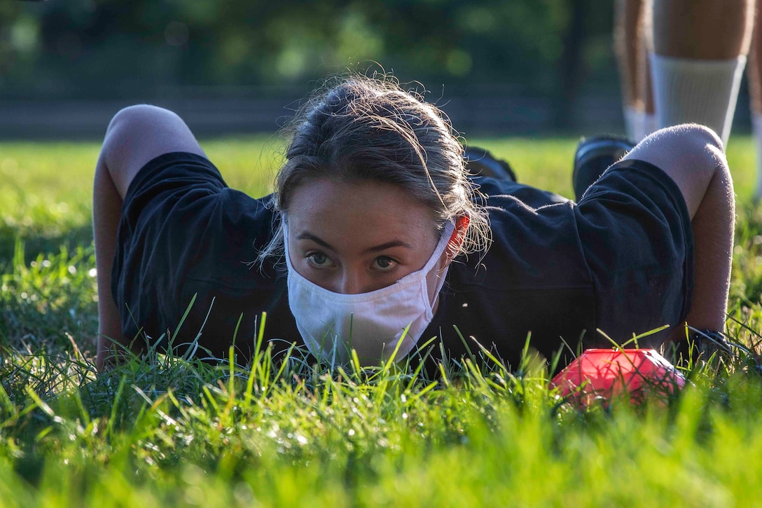 A cadet wearing a face mask does a push up in the grass.