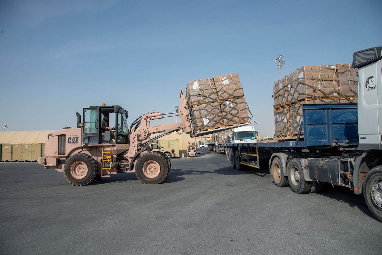 Military personnel use loading equipment to move supplies.