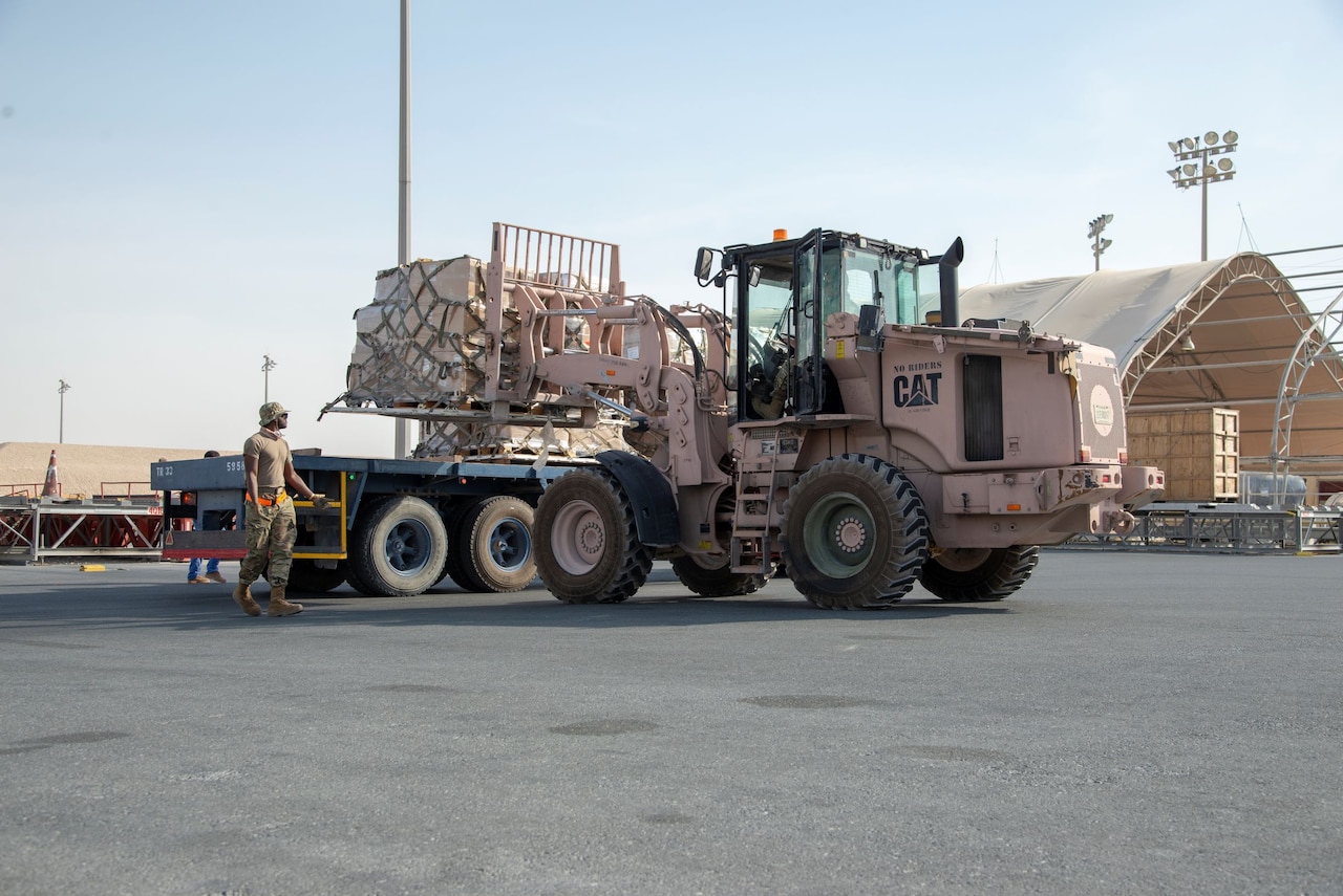 Military personnel use loading equipment to move supplies.