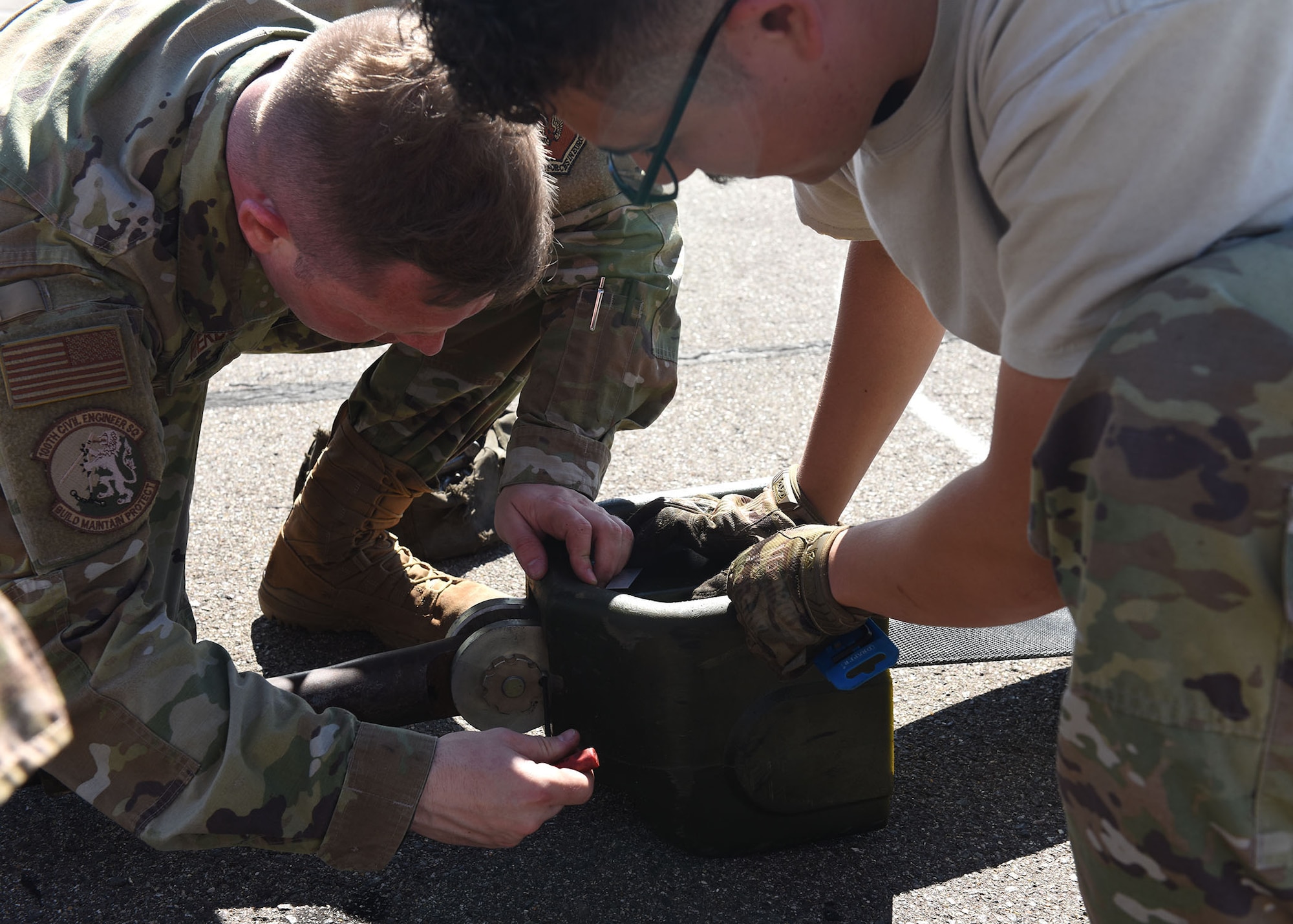 Staff Sgt. David Perdue, left, and Staff Sgt. Erik Rosales, both 100th Civil Engineer Squadron Power Production craftsmen, attach an arresting cable to a cable connector in preparation for raising the cable for barrier maintenance recertification at RAF Mildenhall, England, Aug. 5, 2020. Recertification of the Mobile Aircraft Arresting System is performed annually in addition to daily maintenance checks conducted by power production Airmen 365-days-a-year. (U.S. Air Force photo by Karen Abeyasekere)