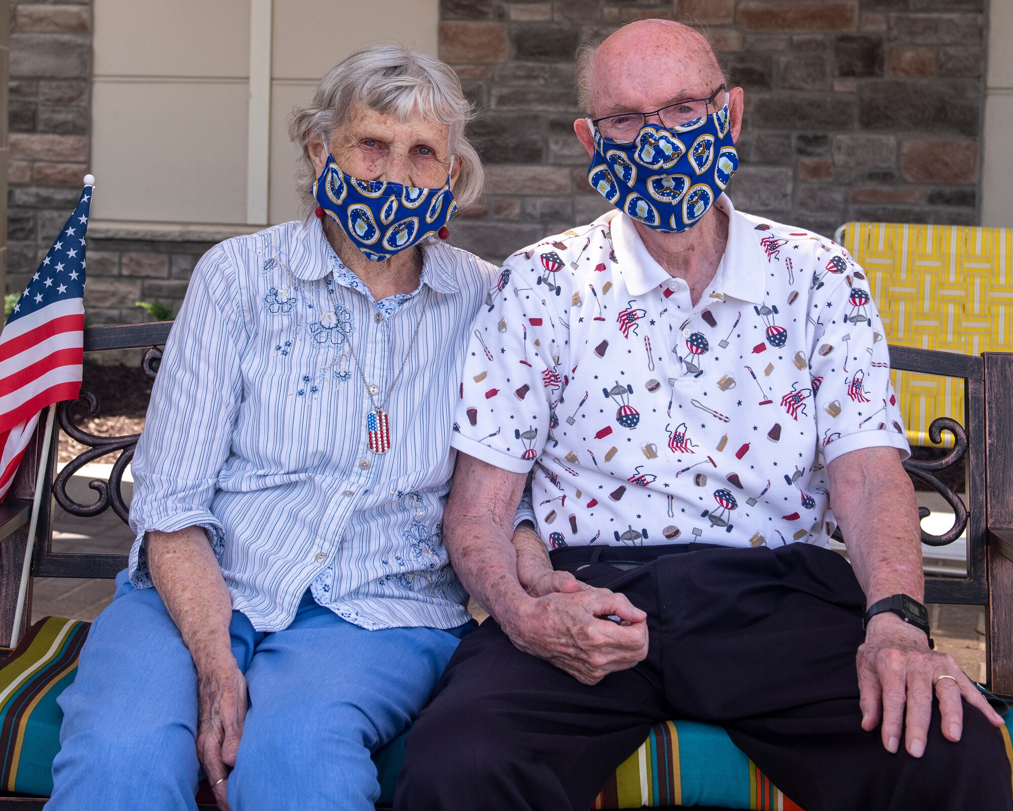 retired Chief Master Sgt. James McCoy and his wife Kathy wearing face masks, holding hands while they sit in front of their home