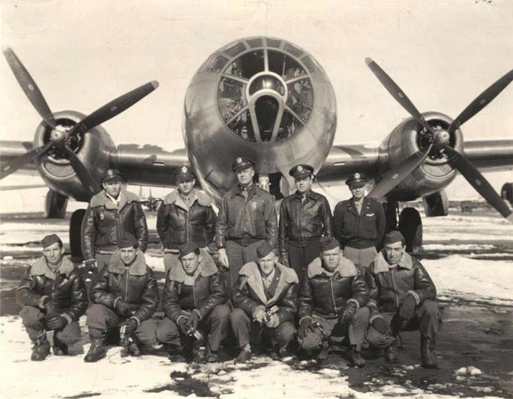 Eleven men pose in front of a B-29 bomber.