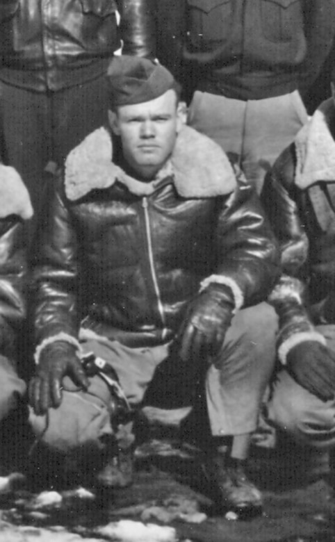 A man squats in a heavy coat and hat.