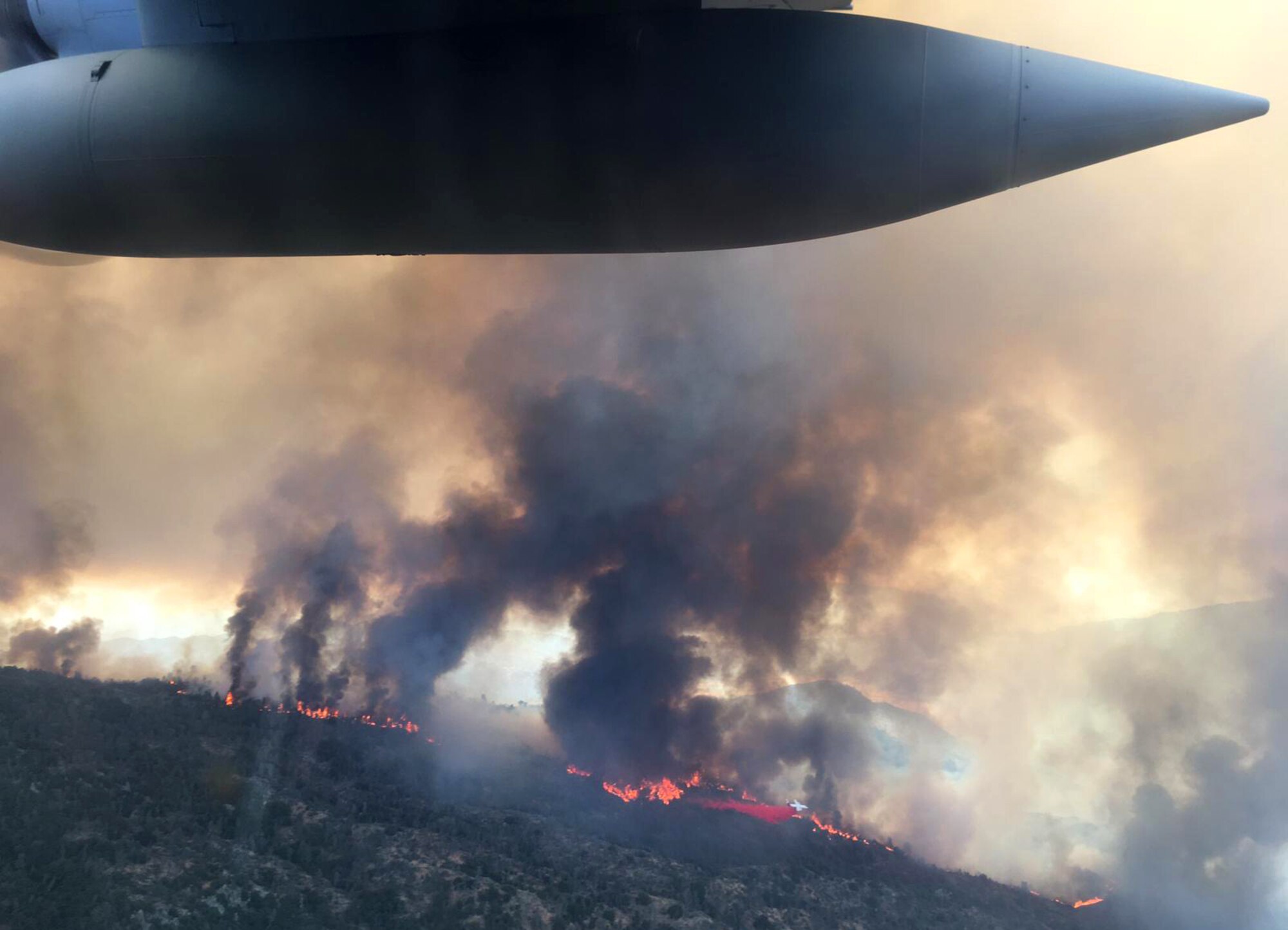 A large military aircraft flies over fires in California.