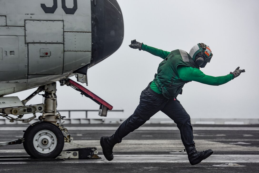 An airman signals an aircraft on a flight deck.