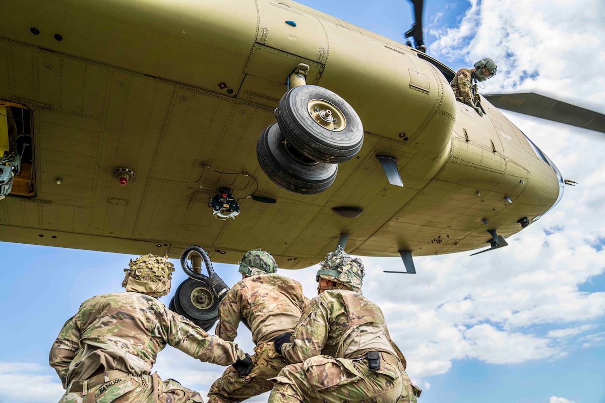 Three soldiers stand underneath a helicopter.